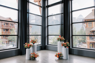 6 flower arrangements vibrant in black compote bowls in front of floor to ceiling windows at main space event center