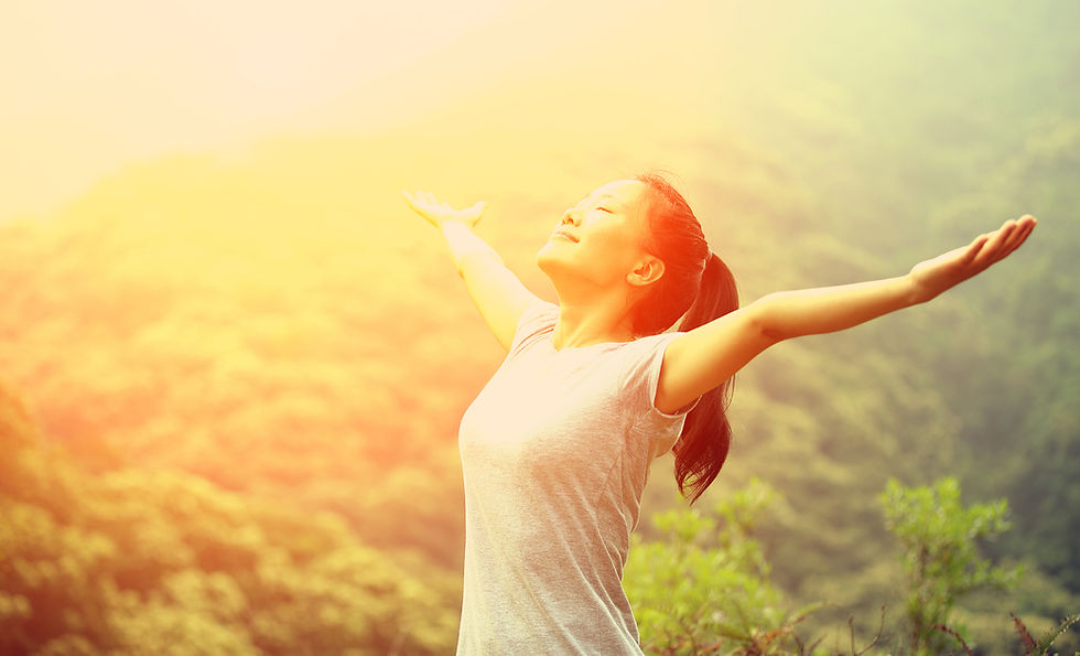Frau steht mit ausgebreiteten Armen im Sonnenlicht vor grüner Natur – Symbol für Dankbarkeit als innere Haltung.