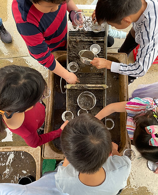 Group of children panning for gold using pans and a sluice.