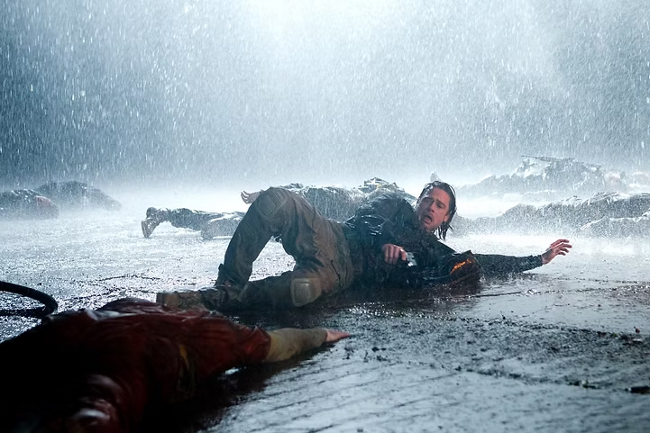 Brad Pitt como Gerry Lane em cena intensa de Guerra Mundial Z, caído no chão sob chuva forte em meio a corpos durante um ataque zumbi