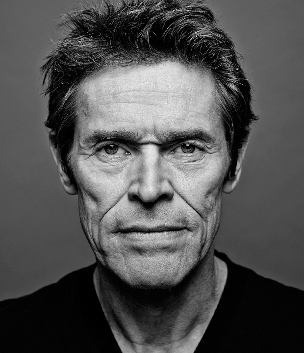 Retrato em preto e branco de Willem Dafoe com expressão séria, cabelo curto e bagunçado, rugas marcantes no rosto e olhar intenso direto para a câmera, sobre fundo neutro.