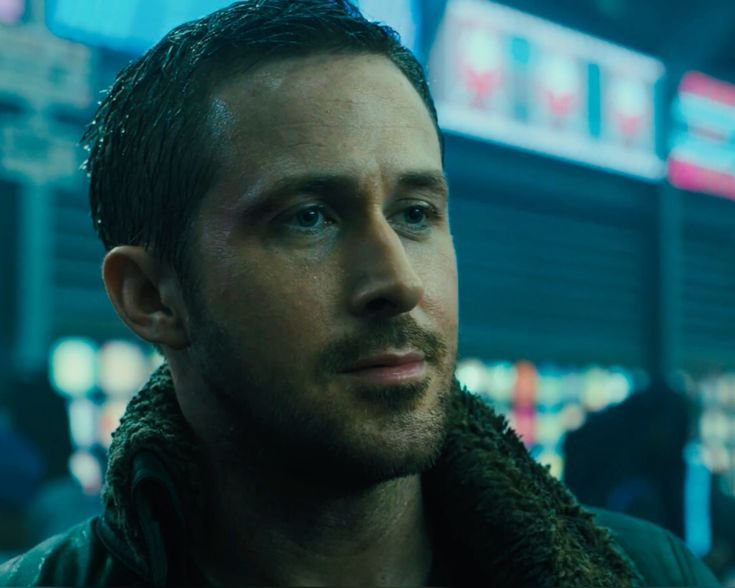 Ryan Gosling como o oficial K no filme Blade Runner 2049, em cena noturna com luzes de neon ao fundo