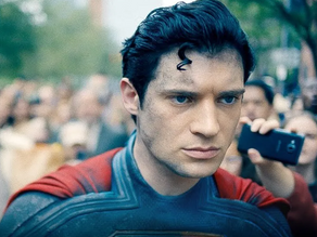 David Corenswet caracterizado como Superman caminha sério em meio a uma multidão, usando o uniforme azul e vermelho no filme dirigido por James Gunn (2025).