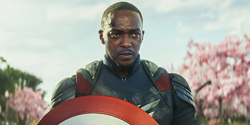 Sam Wilson como o novo Capitão América segurando o escudo em cenário primaveril com flores rosa – personagem do Universo Cinematográfico da Marvel (MCU)