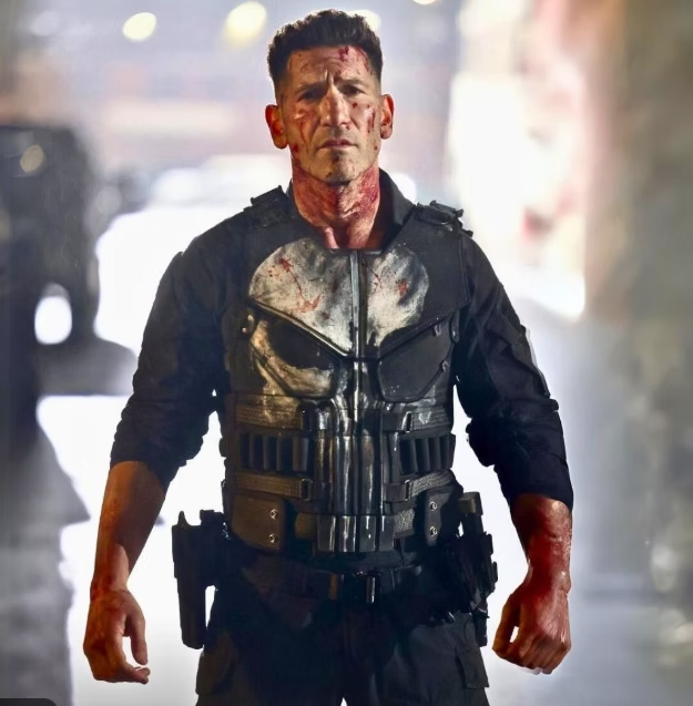Jon Bernthal caracterizado como Justiceiro, com colete tático marcado por sangue e expressão intensa, em cena de ação no revival do personagem pela Marvel.