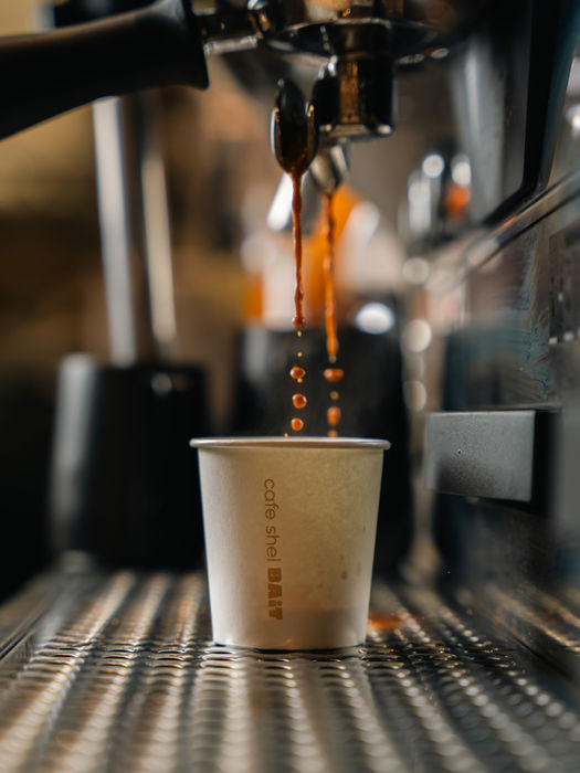 Rich and intense espresso shot in a small glass, served on a saucer with a spoon, at Cafe BAiT, showcasing a thick crema on top and deep, dark color, indicative of its strong flavor.