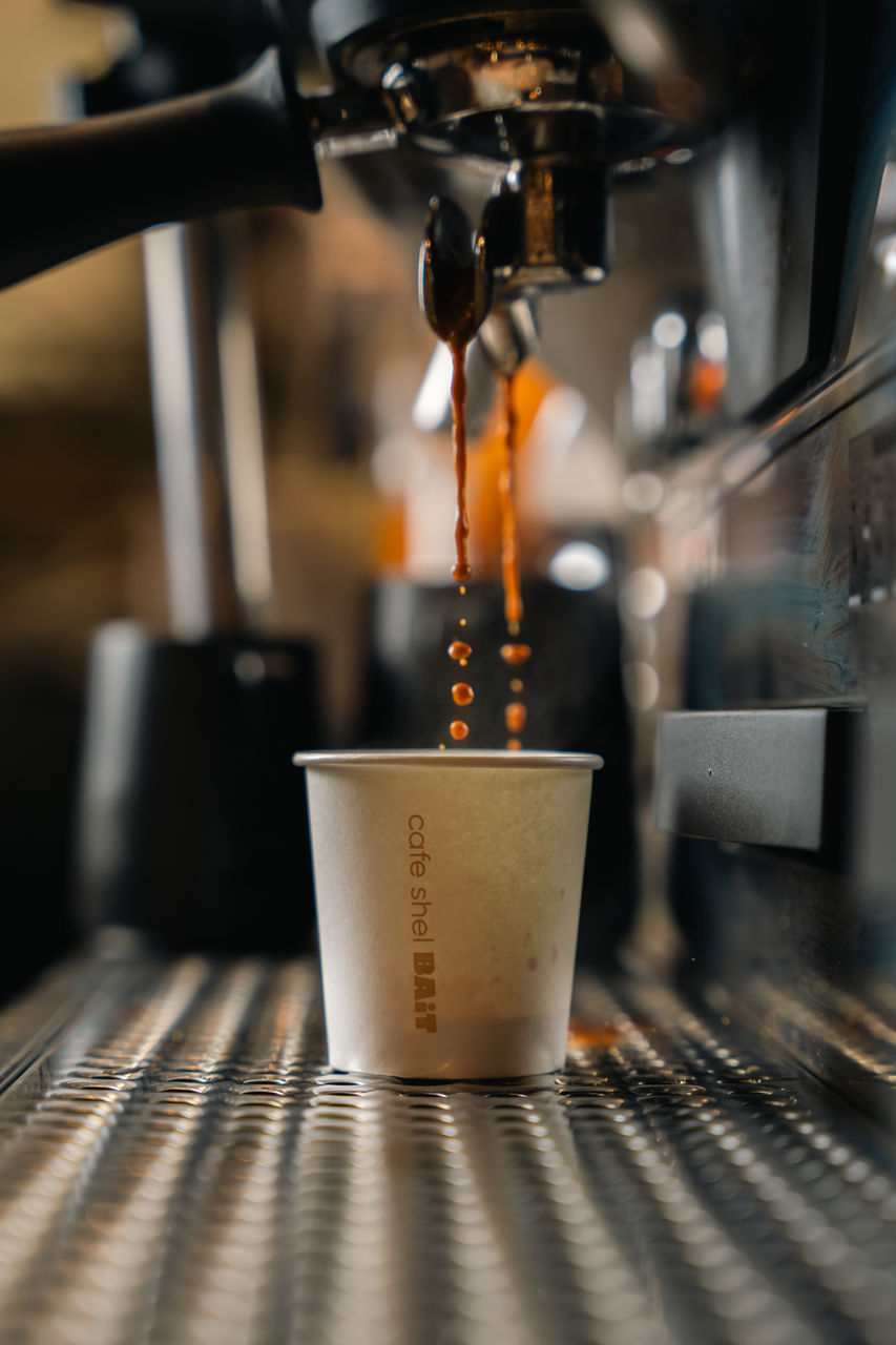 Rich and intense espresso shot in a small glass, served on a saucer with a spoon, at Cafe BAiT, showcasing a thick crema on top and deep, dark color, indicative of its strong flavor.