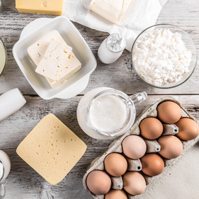 a photo of brown eggs, a carafe of milk, a bowl of cottage cheese, and blocks of cheese on a wooden background