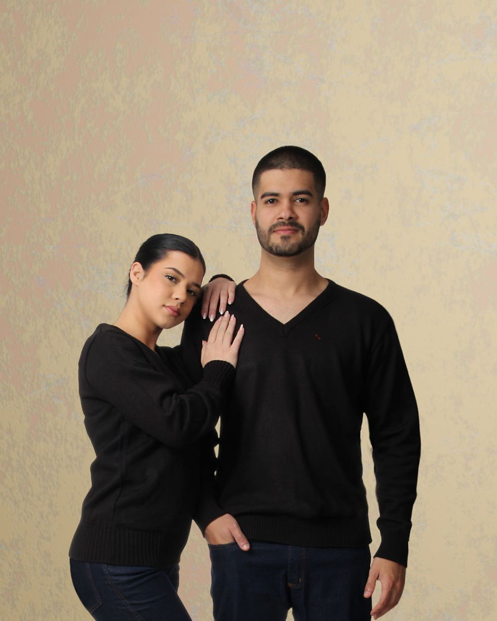 Homem e mulher vestindo suéteres pretos com decote V da SNYG, posando lado a lado em fundo neutro. Roupa casual com elegância