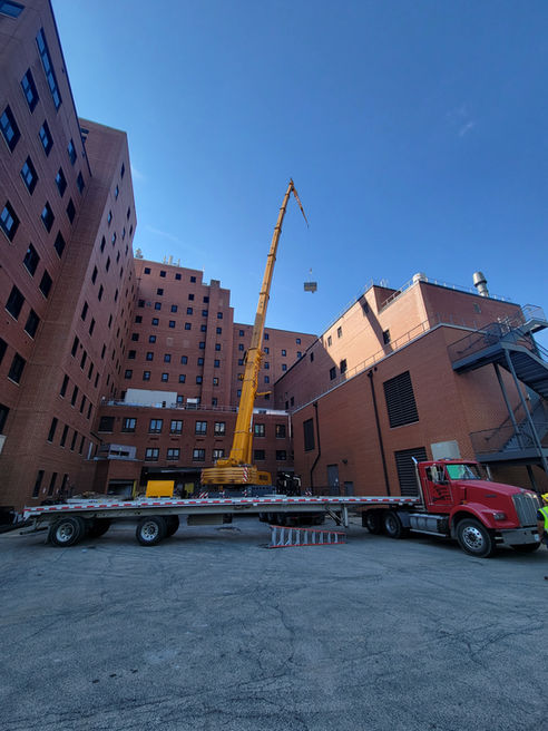 Crane lifting a custom air handling unit over a hospital building during a blind pick at Jesse Brown VA Medical Center, with Roberts HVAC crew guiding the rooftop installation.