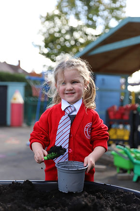 Smiling child in school uniform planting soil in a pot