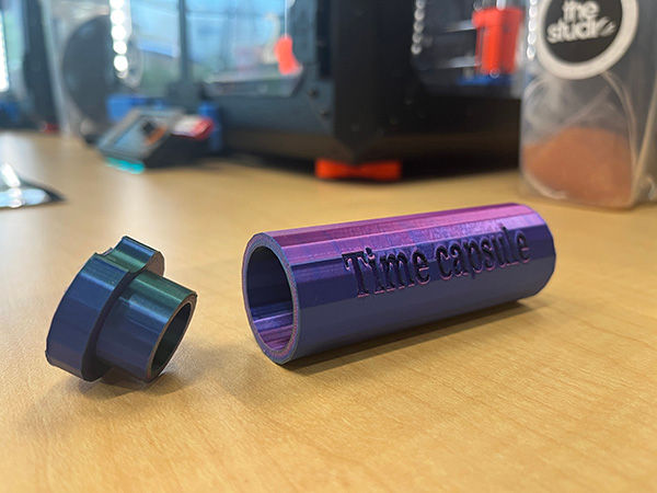 3d-printed time capsule on a work bench with a 3d printer in the background.