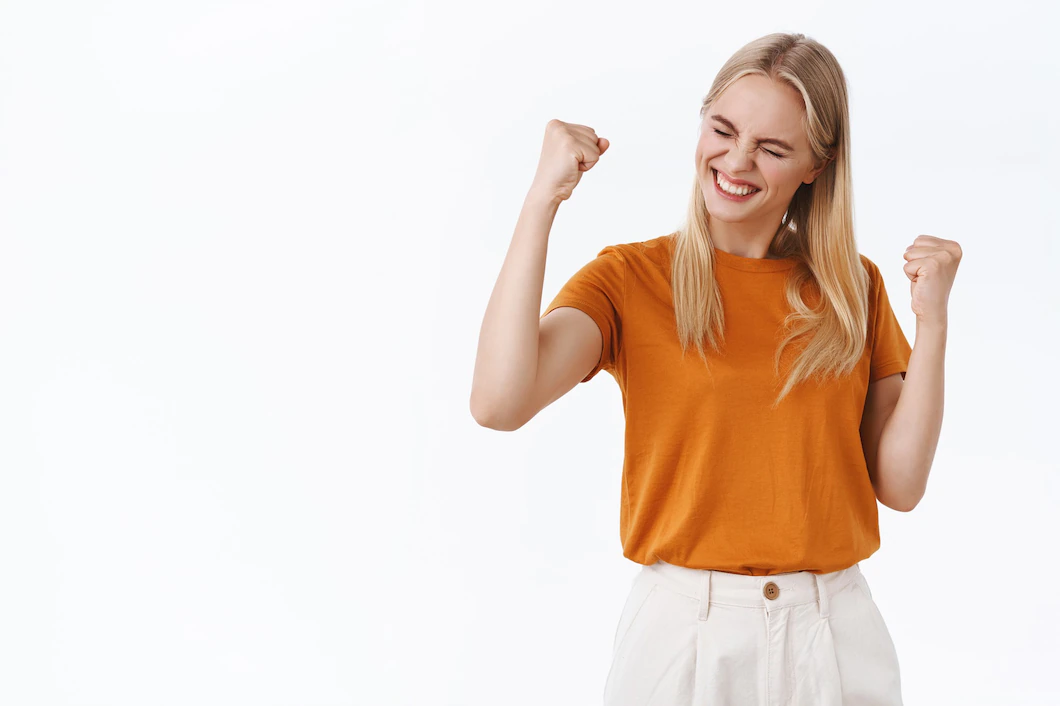 successful-stylish-encouraged-blond-modern-girl-with-tattoos-orange-t-shirt-fist-pump-smil
