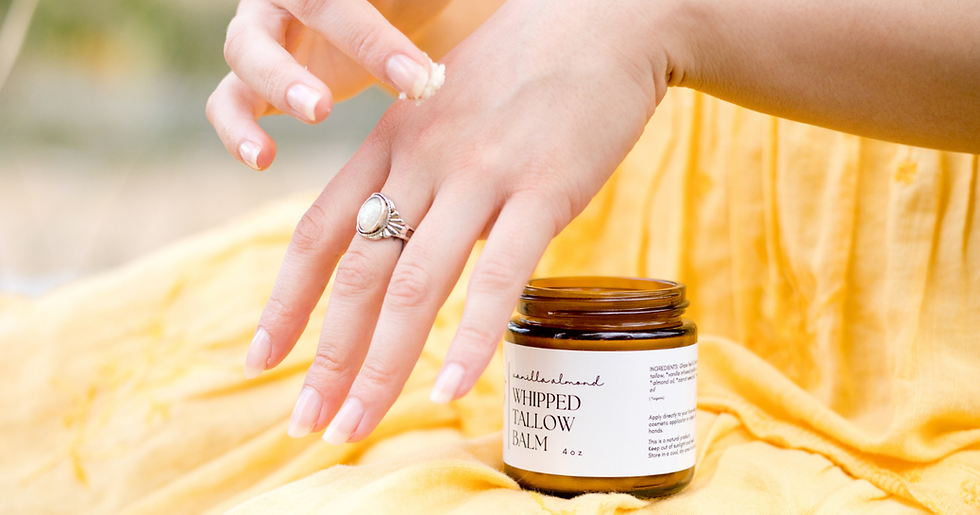 Hands applying whipped tallow balm from an open jar with white label. Background features a soft yellow fabric, creating a warm mood.
