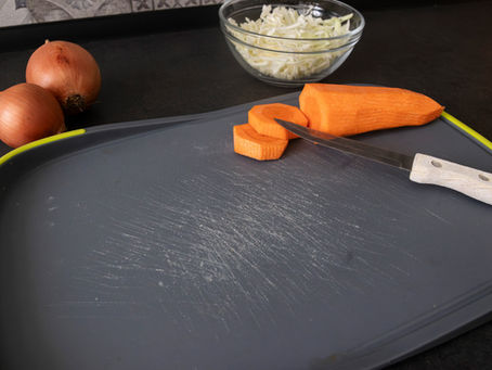 Plastic cutting board showing scratched surface with knife and sliced carrot on it.