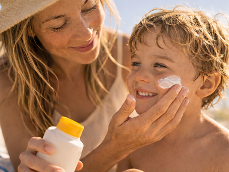 Parent applying sunscreen to a child outdoors on a sunny beach to help protect skin from UV exposure.