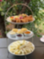 Three-tiered stand with sandwiches, scones, jams, and colorful pastries in a garden setting, creating a cozy afternoon tea vibe.