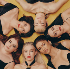 Six young women laying on yellow carpet.
