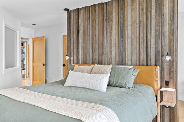 A spacious, modern industrial-style open-concept living area featuring polished concrete floors and warm wood-beamed ceilings with exposed ductwork. The space includes a contemporary kitchen with white cabinetry and a curved breakfast bar, a dining area with a built-in banquette, and a staircase leading to an upper level