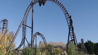 A tall amusement ride at Merlin Theme Parks with a trolley going upside down, against a clear sky