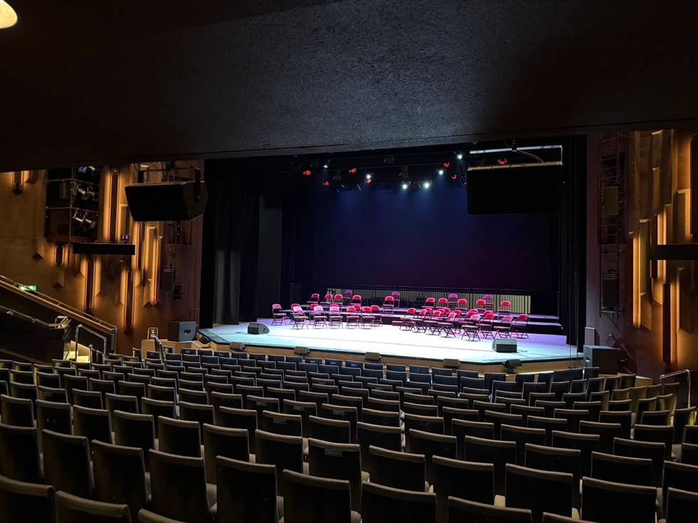 An empty theatre with semi-circles of red chairs spaced on the stage