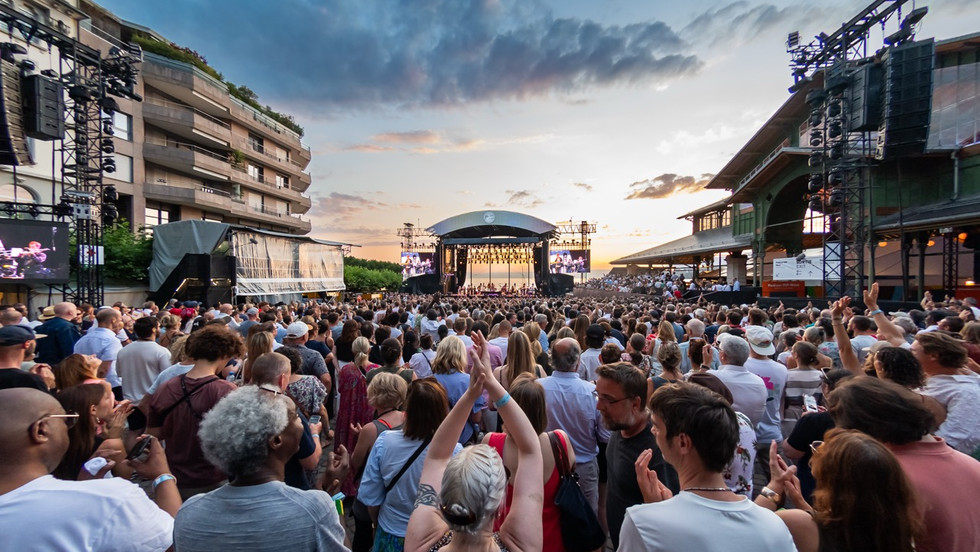 A large crowd in front of an outdoors stage in the distance at the 2025 Montreux Jazz Festival