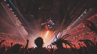 Silhouettes of people dancing at a Linkin Park concert with strobe lighting and a LED box hanging above the crowd