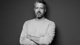 A man with a beard stands looking at the camera with his arms folded. Black-and-white picture