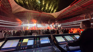 The mixing desk at the back of a filled arena with pyrotechnics at night