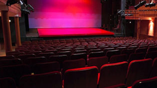 An empty theatre and stage with pink lighting on the stage