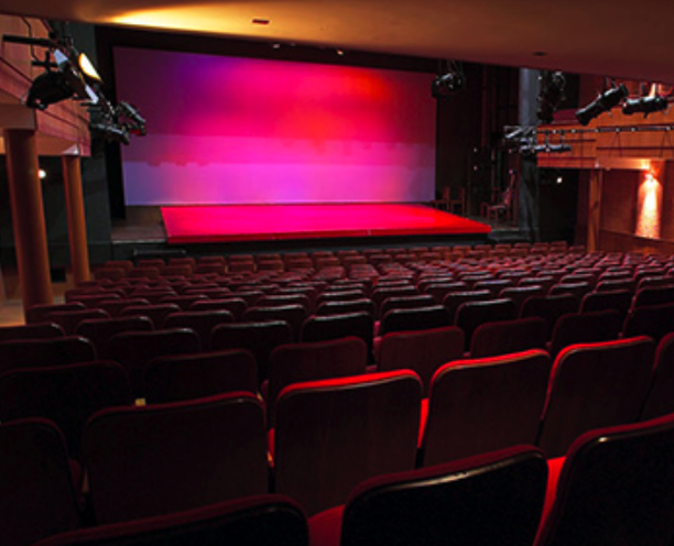 An empty theatre and stage with pink lighting on the stage