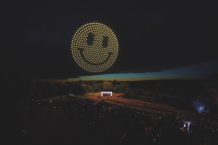 Drones in the night sky making a yellow emoji smiley face in the sky