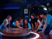 A group of people stand and look at something at a round table in a dark room