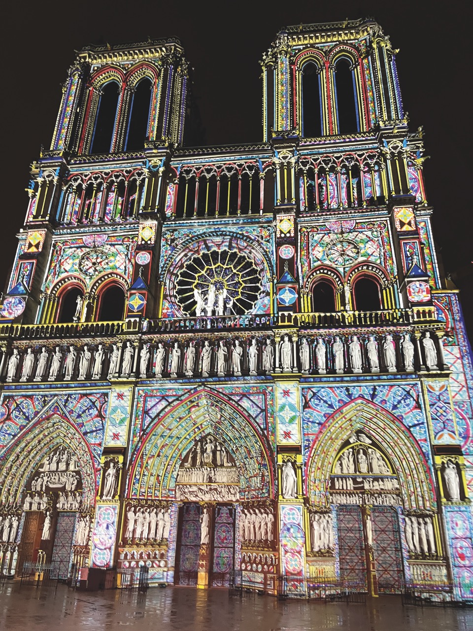 The outside of Notre-Dame de Paris with a projected AV show on the front showing bright colours
