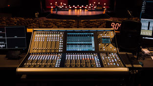 A sound console at the back of an empty auditorium with a glowing stage