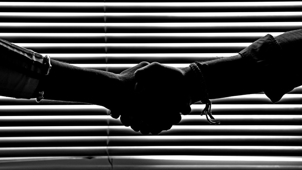 Two people shaking hands in front of blinds, placing them in silhouette