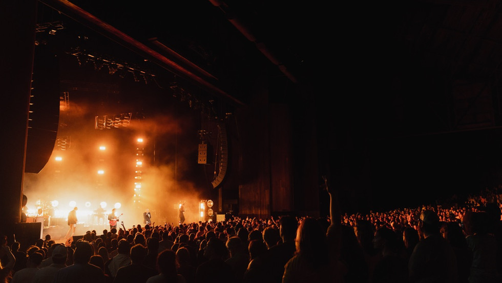 A concert at nighttime with a band playing on an orange-lit stage in front of a large crowd