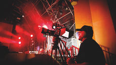 A man wearing a headset looking through a camera at a stage lit in red