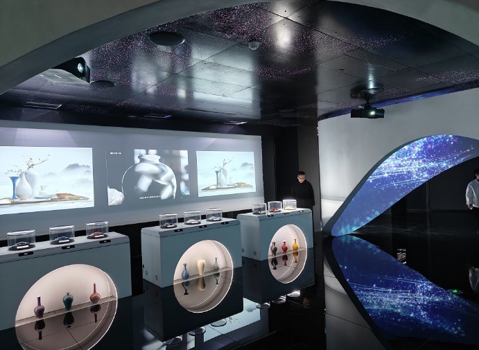 A person standing in an exhibit room with a screen-display in the background and three tables in the middle