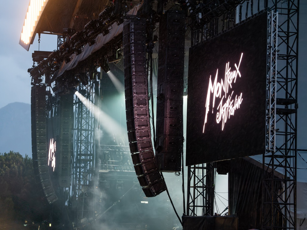 Side view of a hazy stage with large Meyer Sound loudspeakers hanging from the side next to a screen