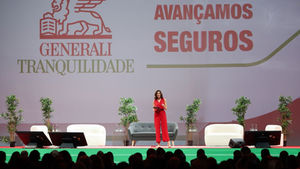 A woman in a red jumpsuit stands on a green stage at Generali Tranquilidade