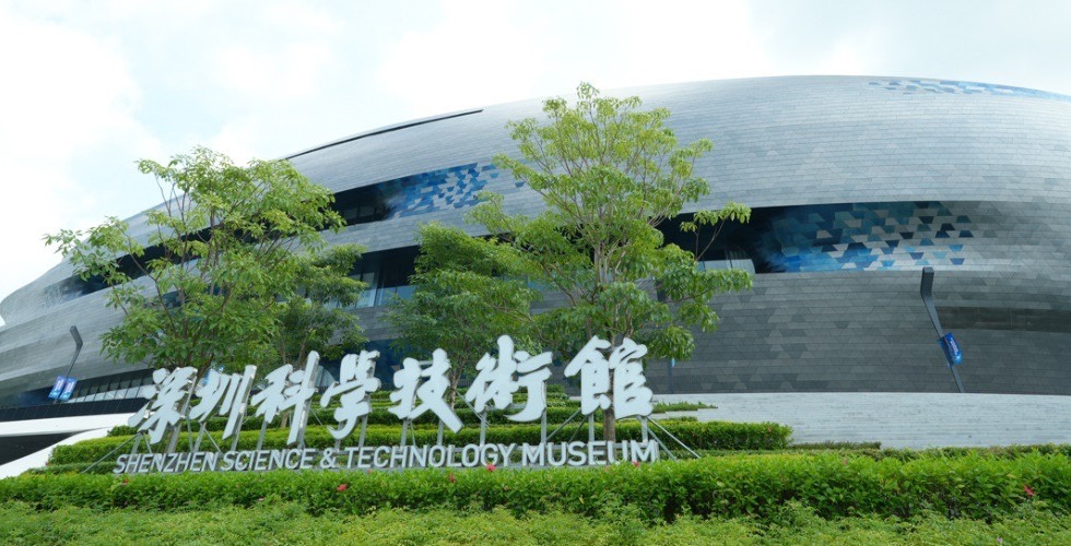 The exterior of Shenzhen Science and Technology Museum with a curved facade and trees in front of the building