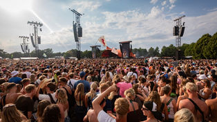 A large crowd at Roskilde Festival 2025 with scaffolding with Meyer Sound loudspeakers on rising above them