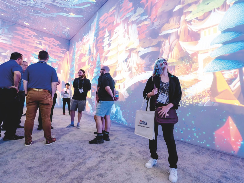 A woman standing and staring up at the ceiling with a smile on her face. She stands in a room with projections on the walls and ceiling with other people