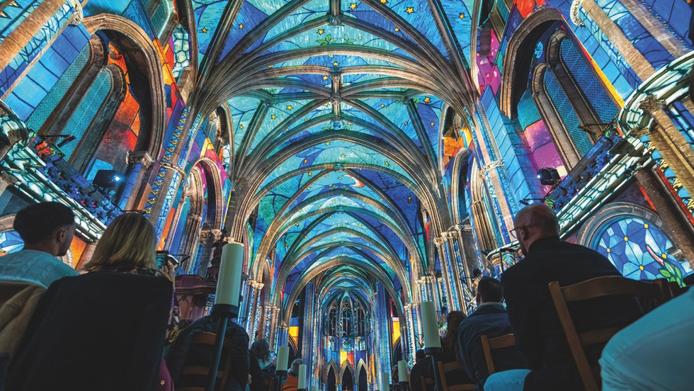 Light projections on the roof of a cathedral with people sitting in the pews