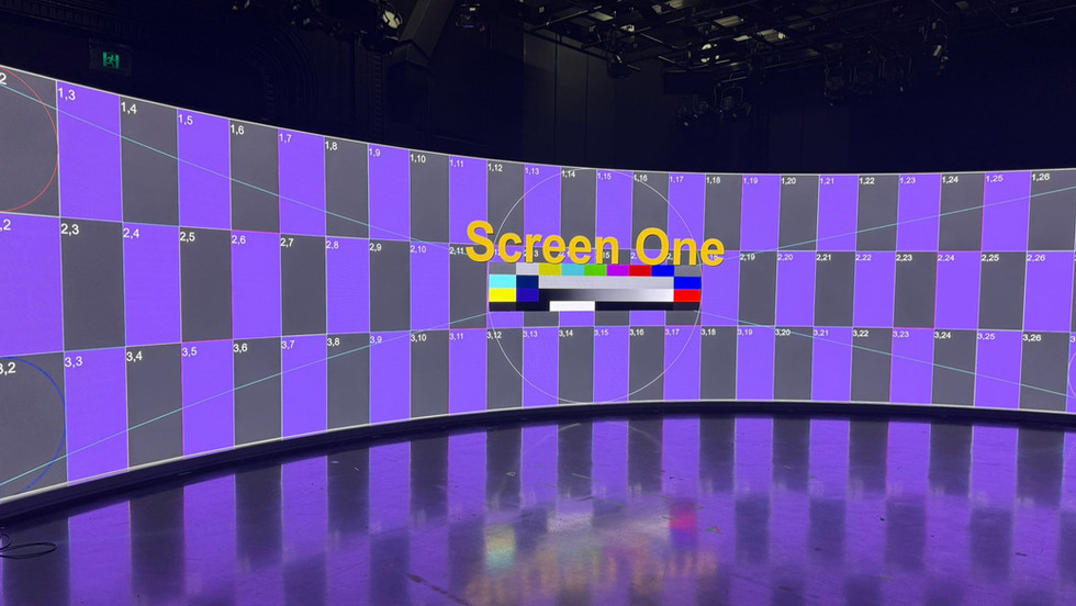 A broadcast studio with a large curved screen showing black and purple squares