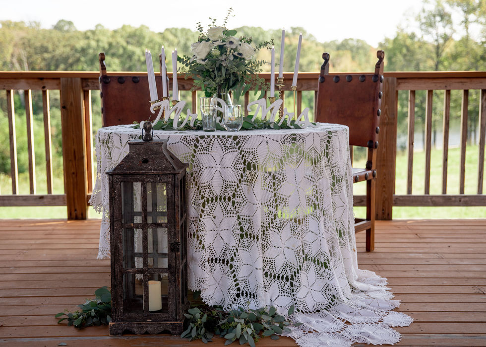 Sweetheart table decorated with lace tablecloth, greenery, and a lantern