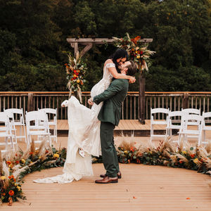 Bride and groom embracing on the wooden ceremony deck at Cedar Cove Ranch with floral arch and string of white chairs