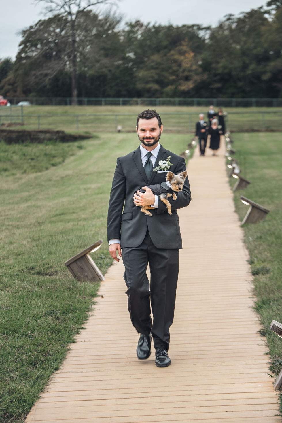 Groomsman in a black suit walking down the aisle path