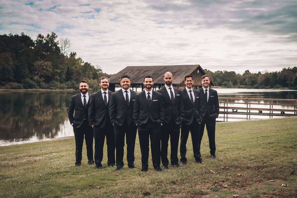 Groomsmen in black suits standing in a line in the field